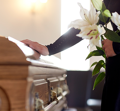 Woman holding flowers in hand and placing other hand on casket