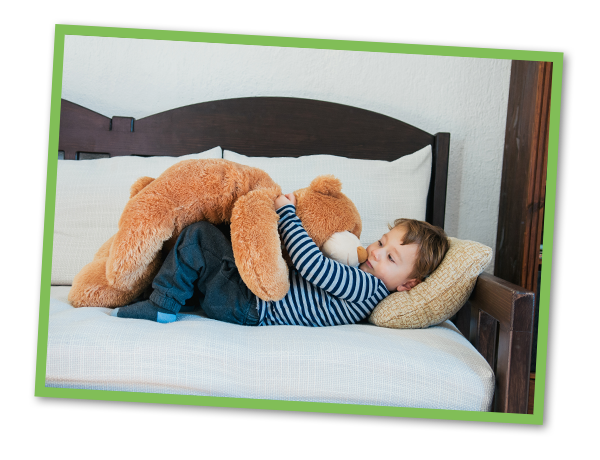 Young boy laying on bed holding big stuffed teddy bear.