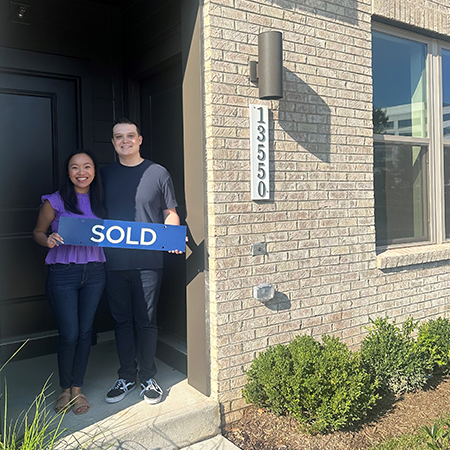 Olivia and Husband holding SOLD sign in entryway of their new house.