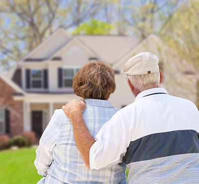 Edlerly couple with backs to camera looking at their home.